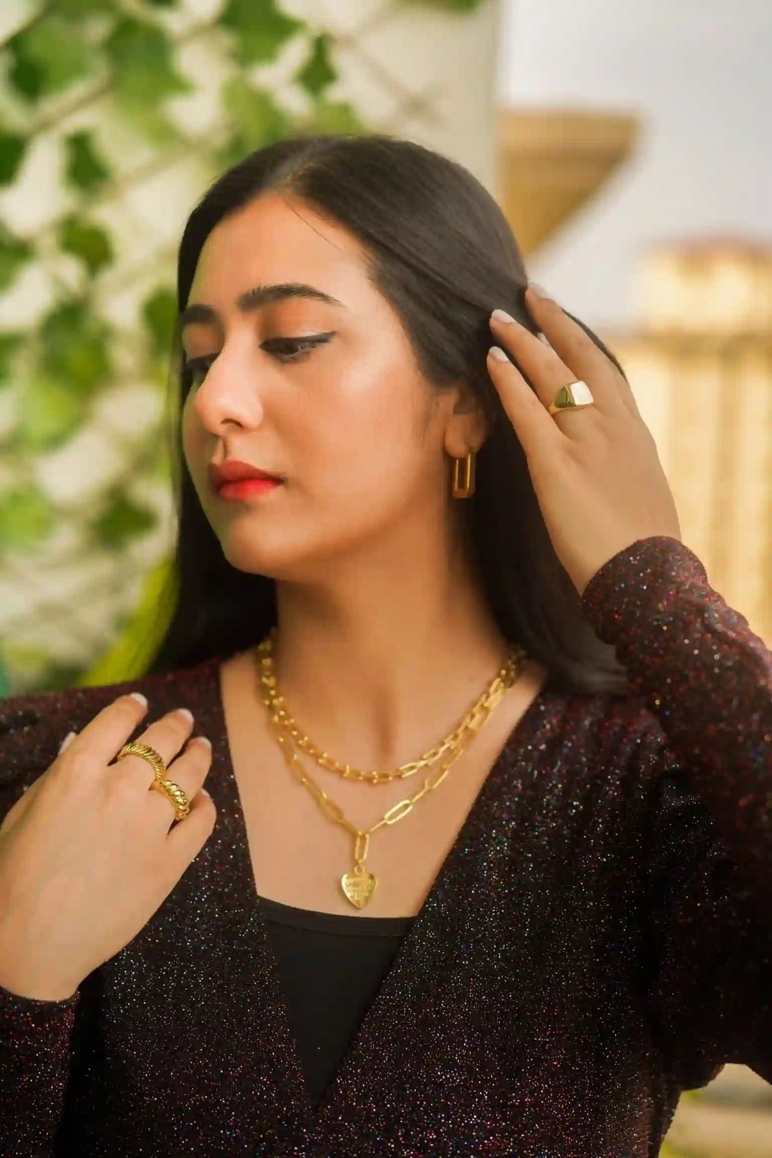 Woman wearing 18k Gold Plated heart pendant necklace, gold rings, and earrings in elegant outfit
