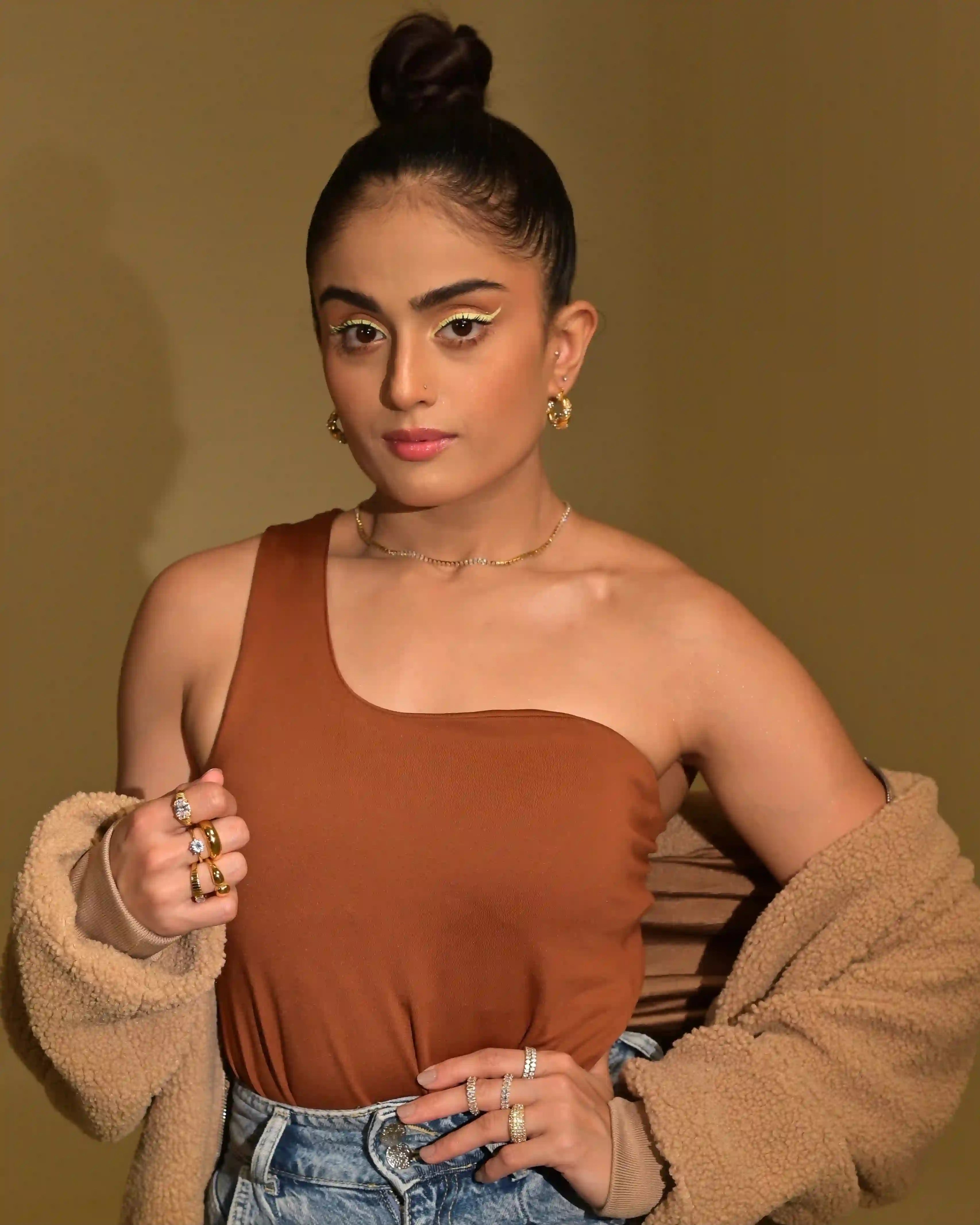 Woman wearing 18k Gold Plated hoop earrings and rings, brown top, and cozy beige jacket