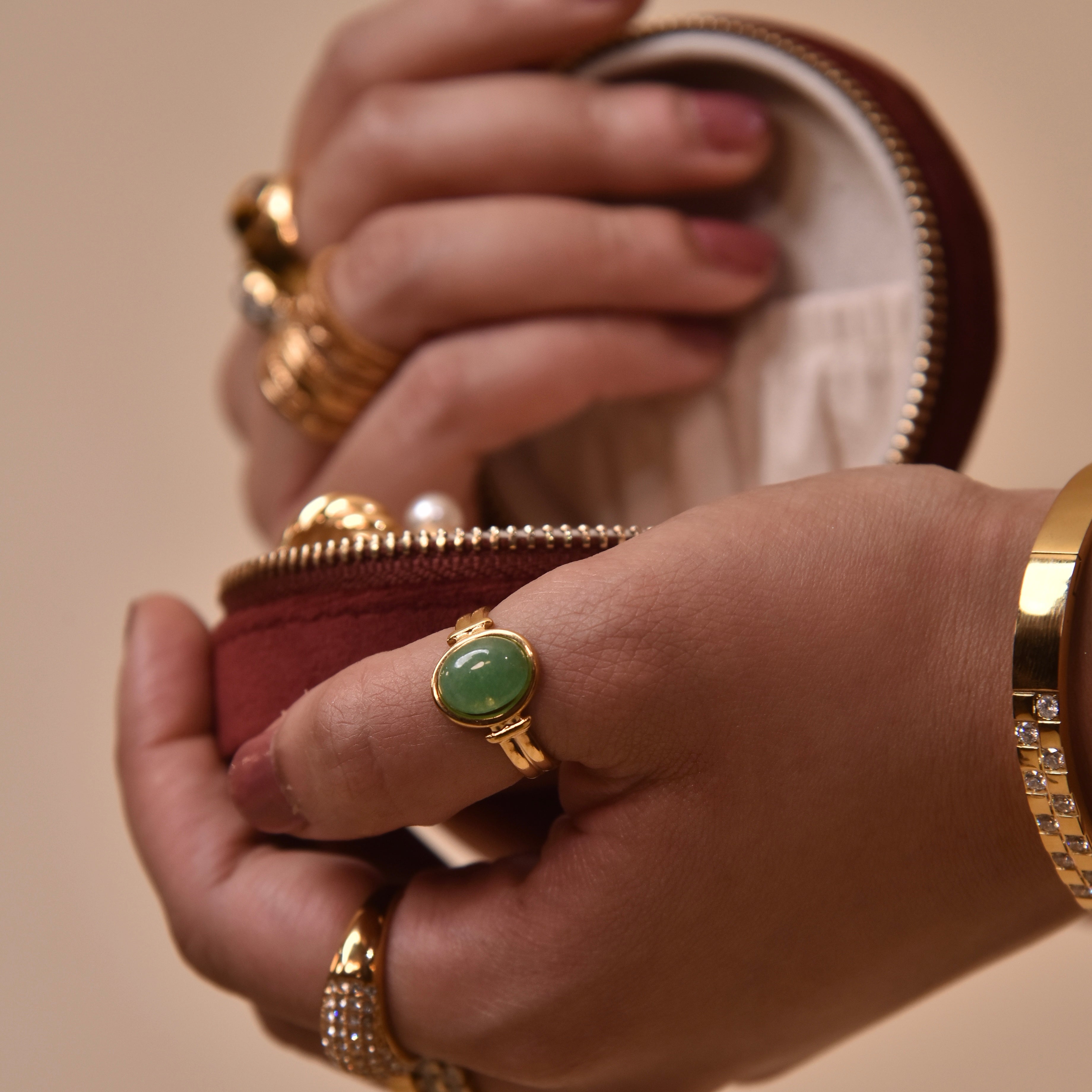 woman wearing 18k Gold Plated green stone ring with gold jewelry holding maroon zip pouch