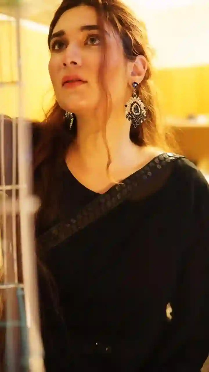 woman wearing black outfit and ornate dangling earrings in warm indoor lighting