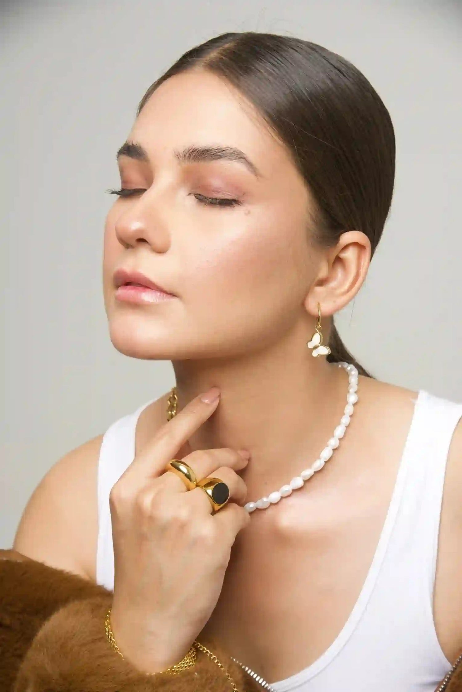 Woman styling in 18k Gold Plated butterfly earrings, pearl necklace, and gold rings with brown fur coat