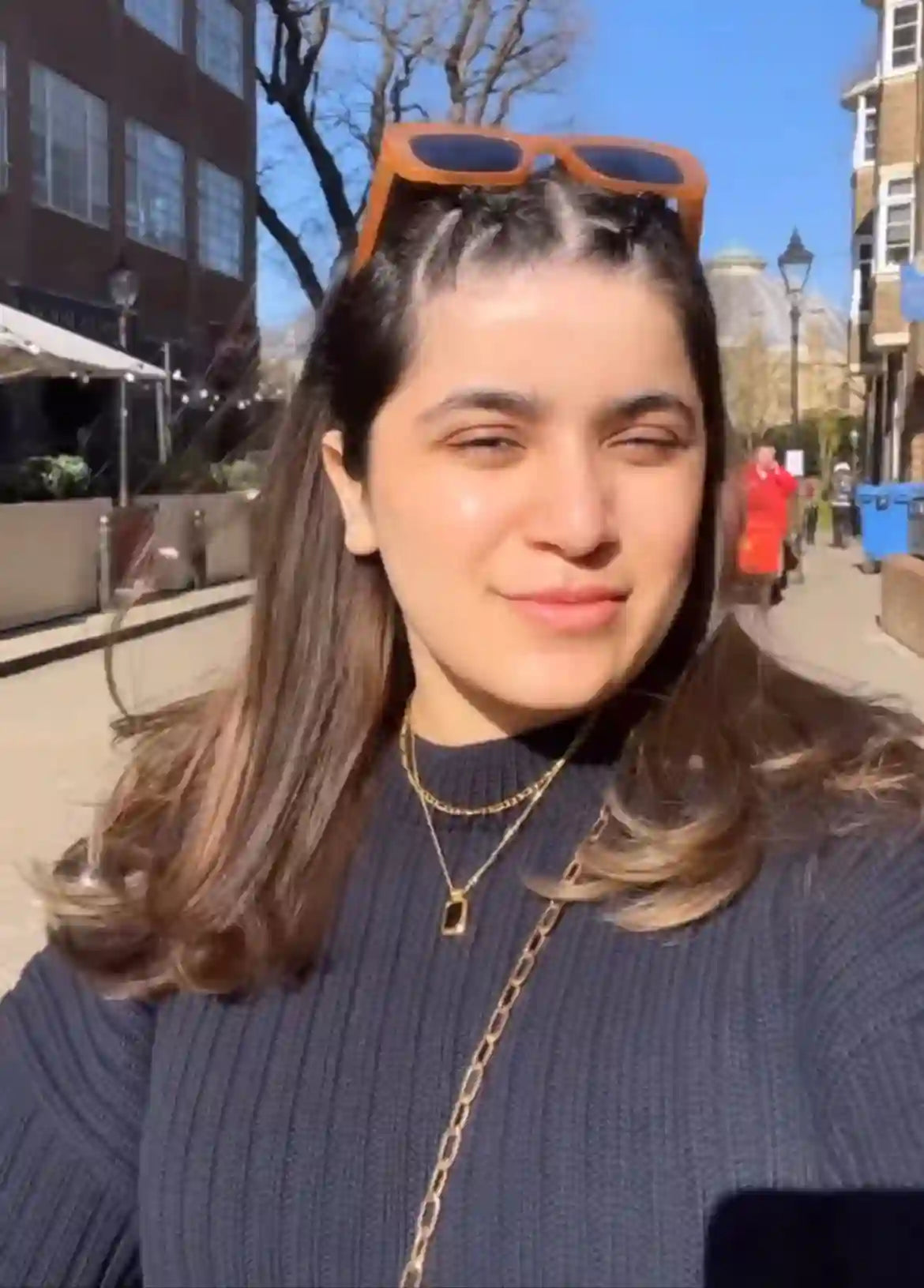 Woman wearing 18k Gold Plated layered necklaces outdoors on a sunny day with orange sunglasses