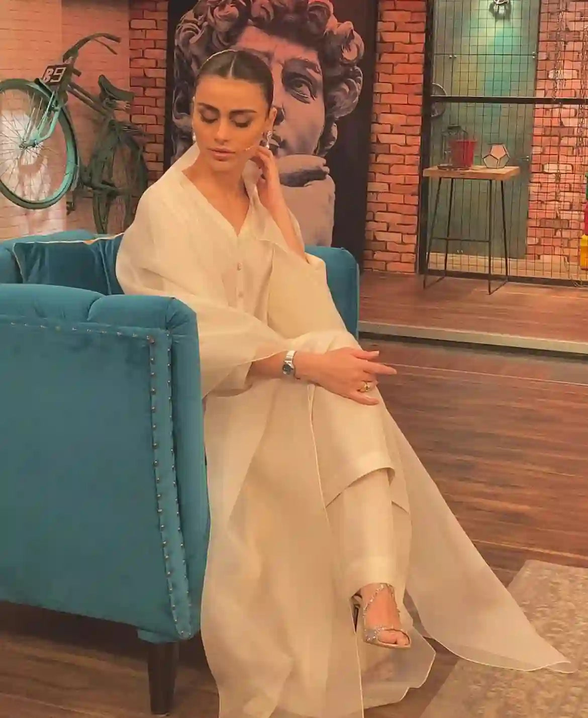 woman wearing 18k Gold Plated earrings sitting on blue chair in modern room with art and bicycle