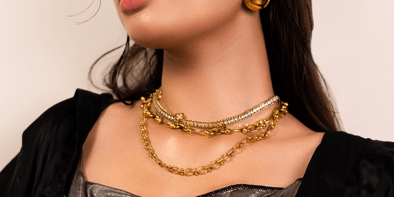 Woman wearing multiple gold necklaces and earrings on a neutral background
